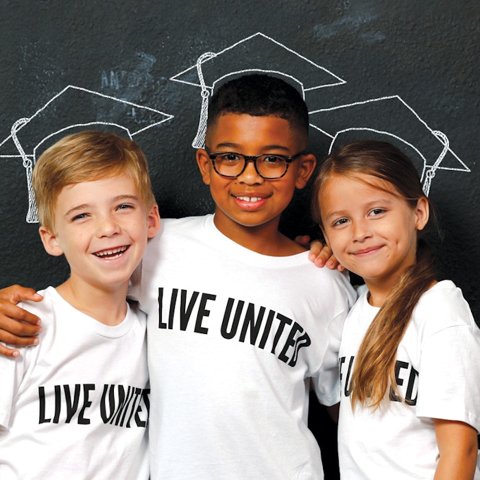 three children in white LIVE UNITED shirts, mortar board chalk outline